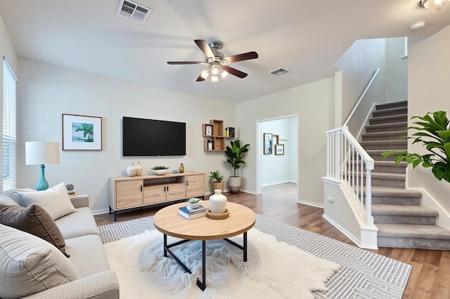 living area with ceiling fan, stairway, visible vents, and wood finished floors