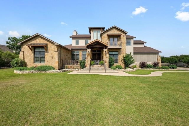 view of front of property featuring a chimney, stone siding, a front lawn, and a balcony