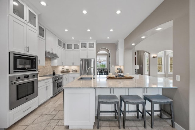 kitchen with a sink, stainless steel appliances, recessed lighting, arched walkways, and decorative backsplash