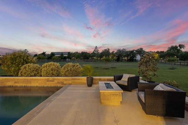 patio terrace at dusk featuring an outdoor living space with a fire pit, fence, and a lawn