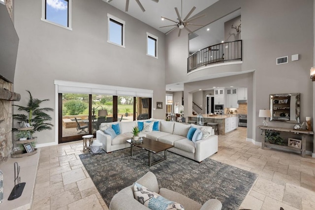 living area featuring visible vents, stone tile floors, ceiling fan, a high ceiling, and baseboards