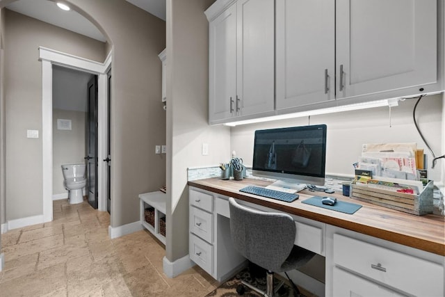 office area featuring built in study area, baseboards, arched walkways, and stone tile floors