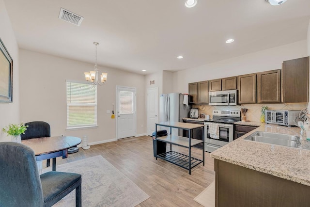 310 Garcitas Creek Ln, Hutto, TX 78634 - kitchen with stainless steel appliances, a chandelier, backsplash, a sink, and hanging light fixtures