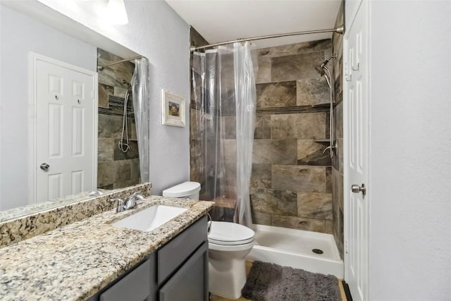 full bath featuring vanity, toilet, a tile shower, and a textured wall