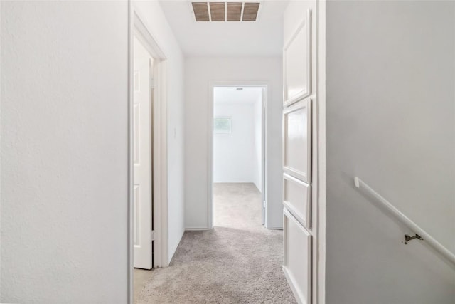 hallway with an upstairs landing, visible vents, and light colored carpet