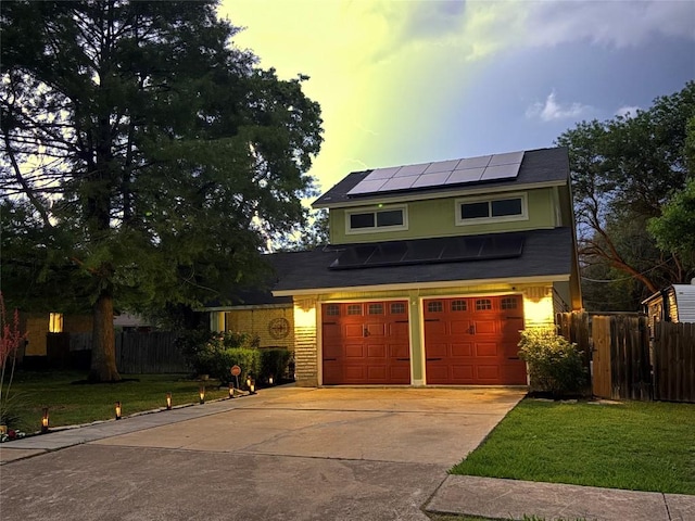 view of front of house with an attached garage, fence, concrete driveway, solar panels, and a front yard