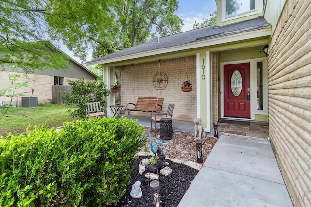 entrance to property featuring central air condition unit, fence, brick siding, and a porch