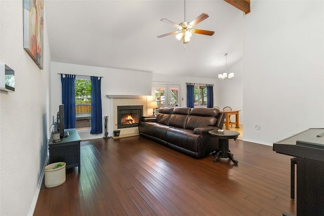 living area with ceiling fan with notable chandelier, high vaulted ceiling, a brick fireplace, dark wood-style floors, and baseboards