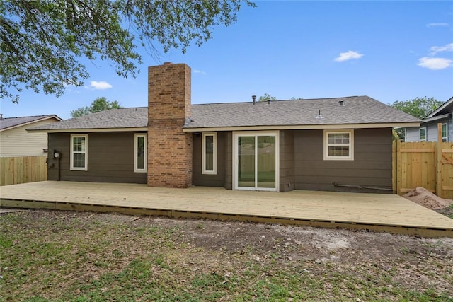 back of property with a shingled roof, a chimney, fence, and a deck