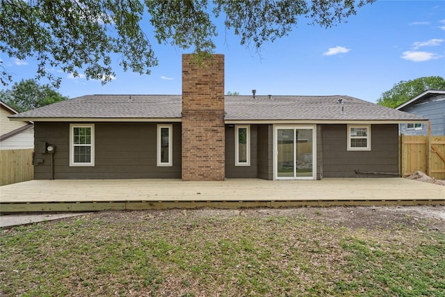 back of house featuring a wooden deck, a chimney, fence, and a lawn