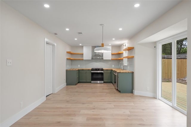 kitchen featuring green cabinets, gas range, open shelves, wall chimney exhaust hood, and backsplash