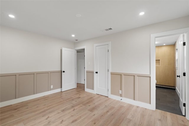 unfurnished bedroom with recessed lighting, a decorative wall, visible vents, and wood finished floors