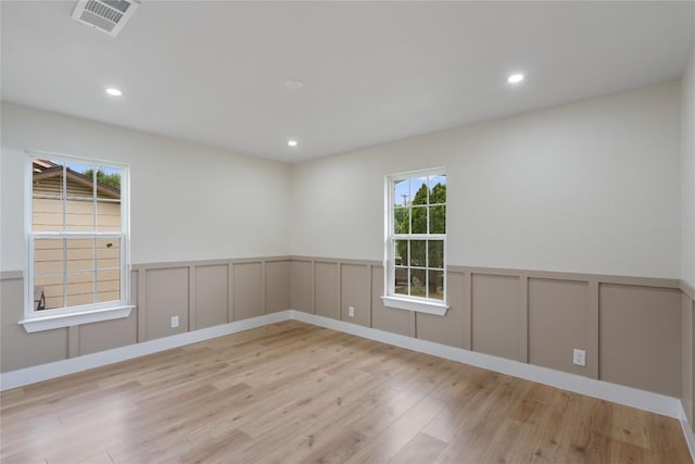 unfurnished room featuring a wealth of natural light, a decorative wall, visible vents, and wood finished floors