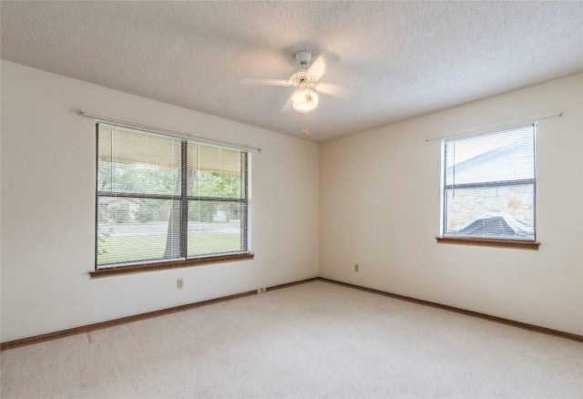 empty room featuring a textured ceiling, light carpet, baseboards, and a ceiling fan