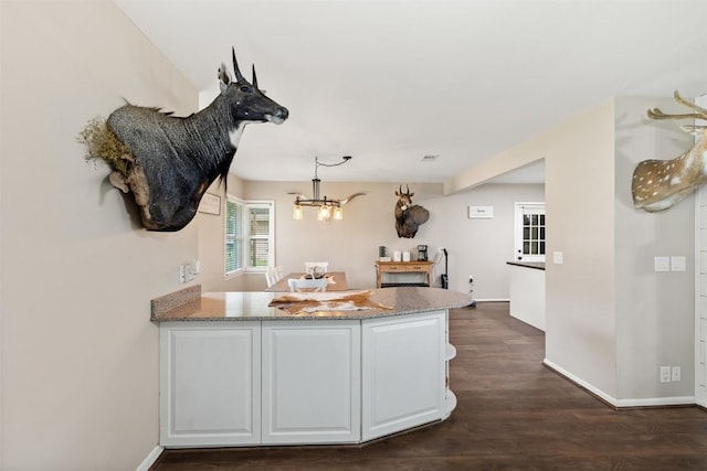 kitchen with light stone countertops, dark wood finished floors, a peninsula, a chandelier, and white cabinets