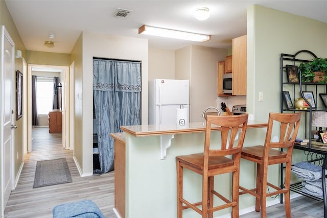 kitchen with freestanding refrigerator, light wood-type flooring, visible vents, and stainless steel microwave