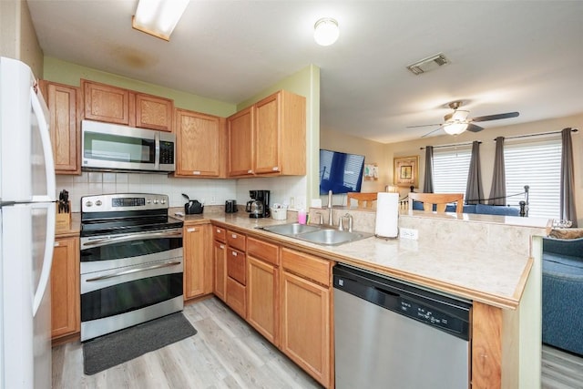kitchen with a peninsula, a sink, appliances with stainless steel finishes, visible vents, and light wood-style floors