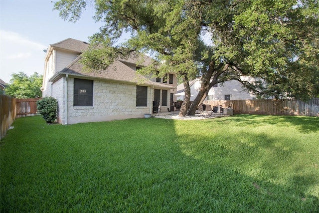 rear view of property with a yard, stone siding, roof with shingles, and a fenced backyard