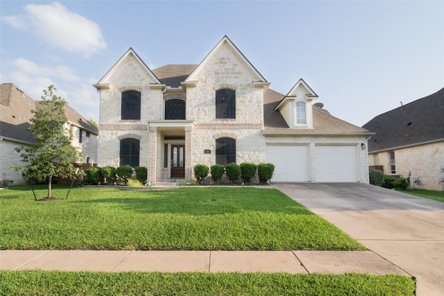 french country home with driveway, a front yard, a garage, stone siding, and roof with shingles