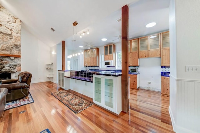 3701 Fischer Store Rd, Wimberley, TX 78676 - kitchen featuring white microwave, light wood finished floors, tile countertops, and glass insert cabinets