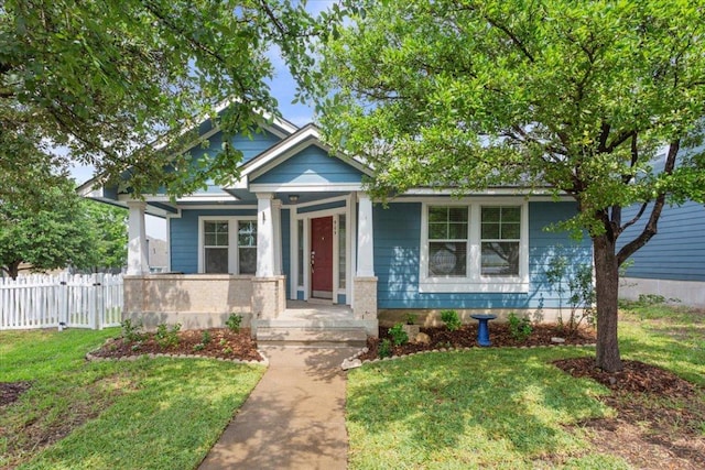 view of front of property featuring covered porch, fence, and a front lawn