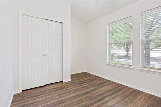 unfurnished bedroom featuring baseboards, lofted ceiling, a closet, and dark wood-style floors
