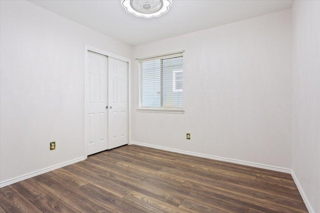 unfurnished bedroom featuring baseboards, dark wood-type flooring, and a closet