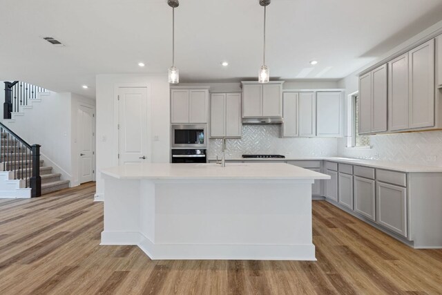 565 Raleigh Dr, Georgetown, TX 78633 - kitchen with gray cabinetry, wall oven, under cabinet range hood, light wood-type flooring, and light countertops