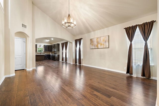unfurnished living room featuring a notable chandelier, arched walkways, visible vents, and dark wood finished floors