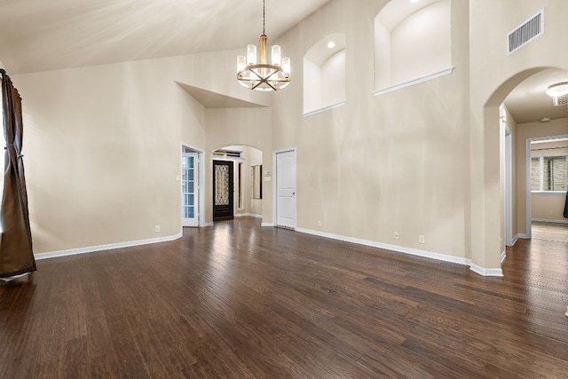 unfurnished living room featuring wood finished floors, a towering ceiling, visible vents, an inviting chandelier, and arched walkways