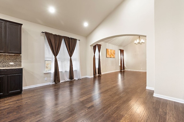 unfurnished living room with baseboards, dark wood finished floors, an inviting chandelier, vaulted ceiling, and arched walkways