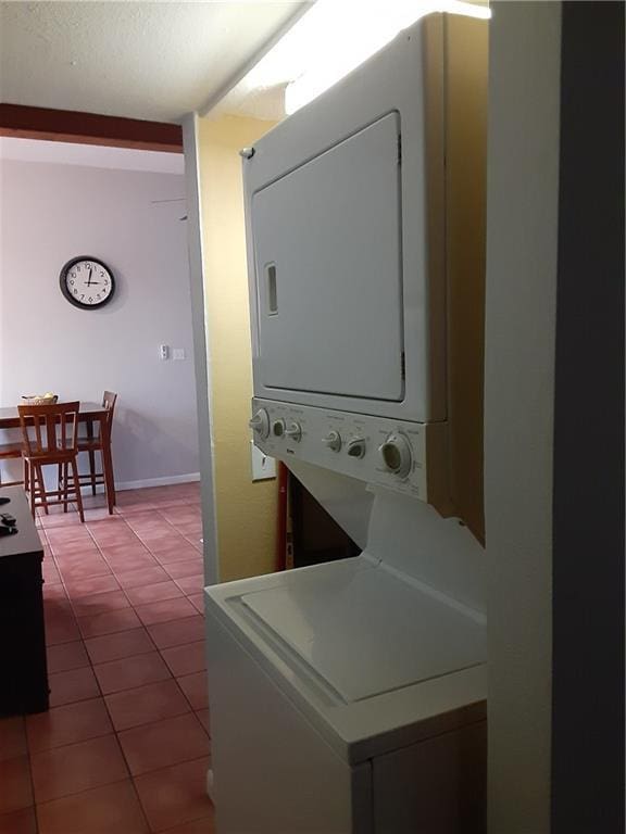 laundry area featuring baseboards, stacked washer and dryer, laundry area, and tile patterned flooring