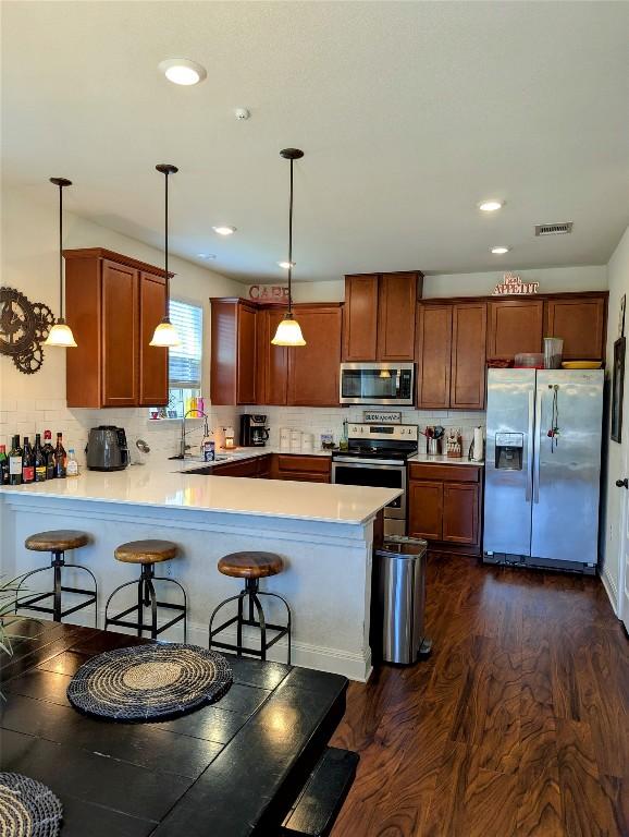 7617 Rio Pass, Austin, TX 78724 - kitchen with appliances with stainless steel finishes, a peninsula, light countertops, pendant lighting, and backsplash