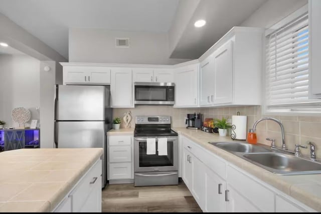 102 W Corral St Unit 2, South Padre Island, TX 78597 - kitchen featuring stainless steel appliances, tile countertops, white cabinets, light wood-style flooring, and decorative backsplash