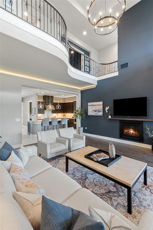 1300 Morning Moon Cir, Austin, TX 78732 - living room featuring a chandelier, wood finished floors, a towering ceiling, a glass covered fireplace, and baseboards