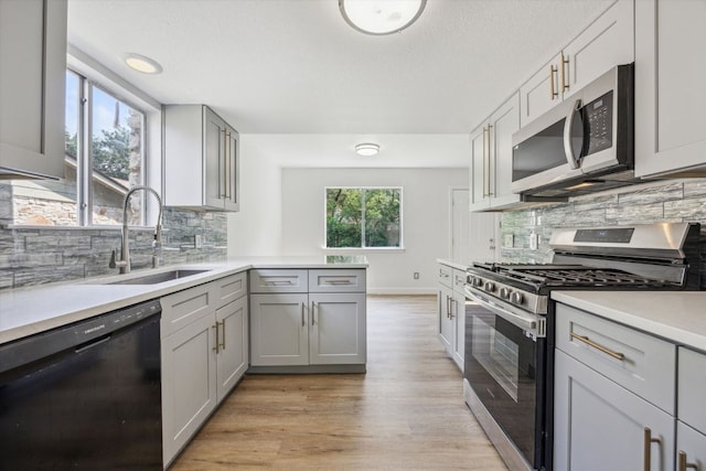 kitchen with a sink, light wood finished floors, light countertops, gray cabinetry, and appliances with stainless steel finishes