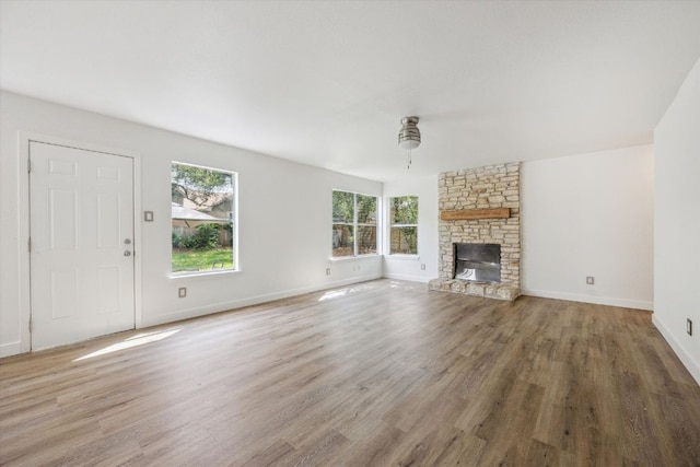 unfurnished living room with a wealth of natural light, baseboards, a stone fireplace, and wood finished floors