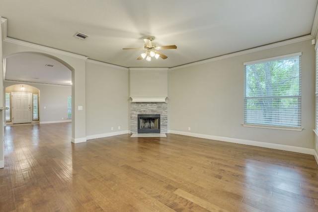unfurnished living room featuring ceiling fan, wood finished floors, arched walkways, baseboards, and ornamental molding