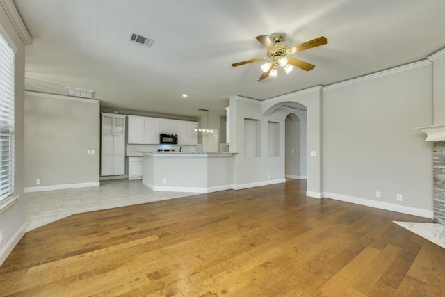 unfurnished living room with ceiling fan, arched walkways, light wood-style floors, baseboards, and ornamental molding