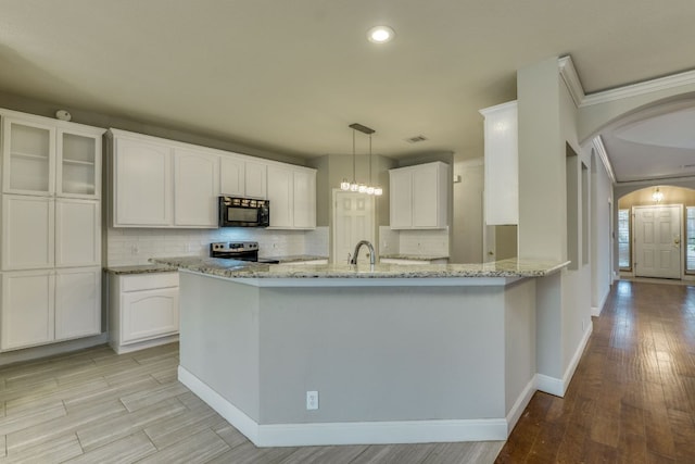kitchen with black microwave, electric stove, arched walkways, light wood finished floors, and decorative backsplash