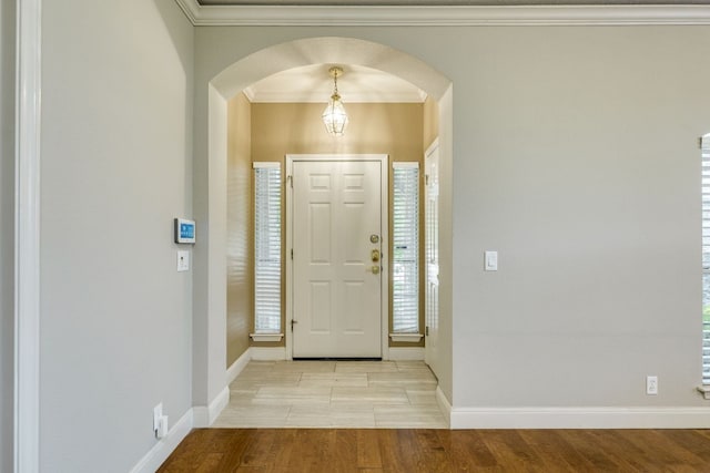 foyer entrance with arched walkways, wood finished floors, ornamental molding, baseboards, and healthy amount of natural light