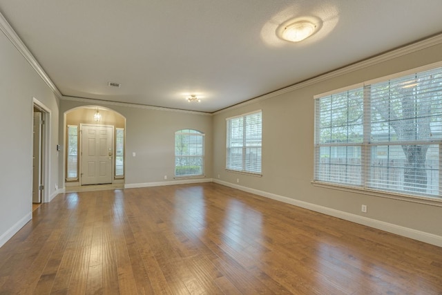 empty room featuring arched walkways, wood finished floors, ornamental molding, and baseboards