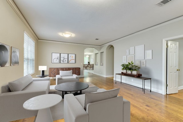 living area featuring arched walkways, light wood-style flooring, crown molding, and baseboards