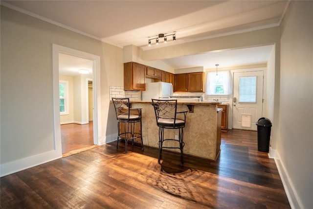 kitchen with a peninsula, brown cabinets, freestanding refrigerator, a kitchen bar, and plenty of natural light