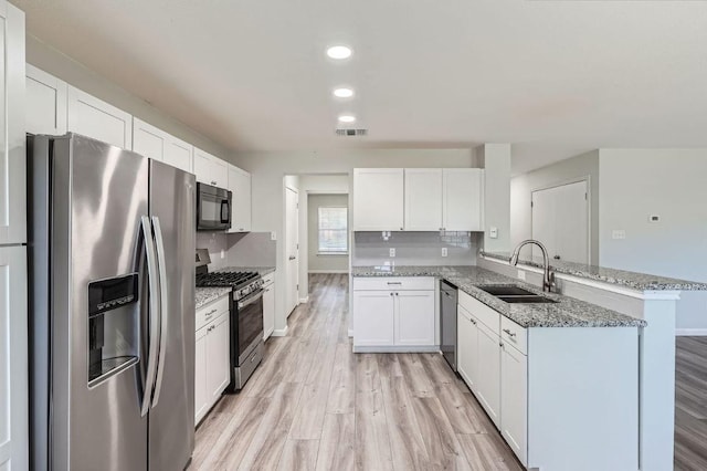 305 Bird Dog Bnd, Bastrop, TX 78602 - kitchen with appliances with stainless steel finishes, a sink, a peninsula, light wood-style floors, and white cabinets