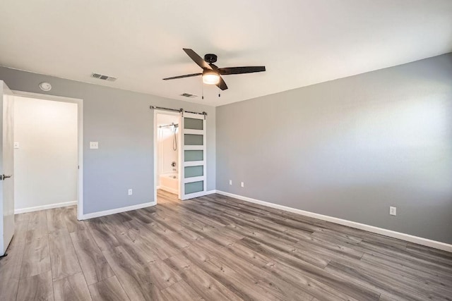 305 Bird Dog Bnd, Bastrop, TX 78602 - unfurnished bedroom with wood finished floors, a barn door, baseboards, a ceiling fan, and connected bathroom