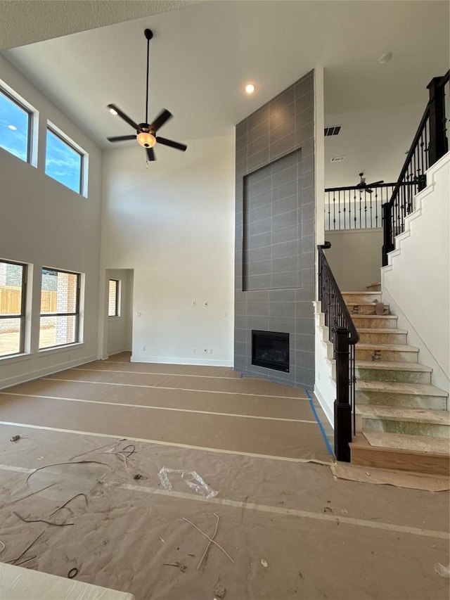 1033 Blanket Flower Dr, Georgetown, TX 78628 - unfurnished living room featuring a tile fireplace, baseboards, ceiling fan, stairway, and a high ceiling