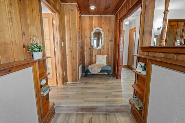 hall featuring wooden walls, light wood finished floors, and wooden ceiling
