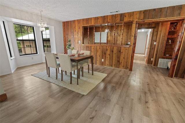 dining room with a chandelier, light wood-style floors, visible vents, and wooden walls