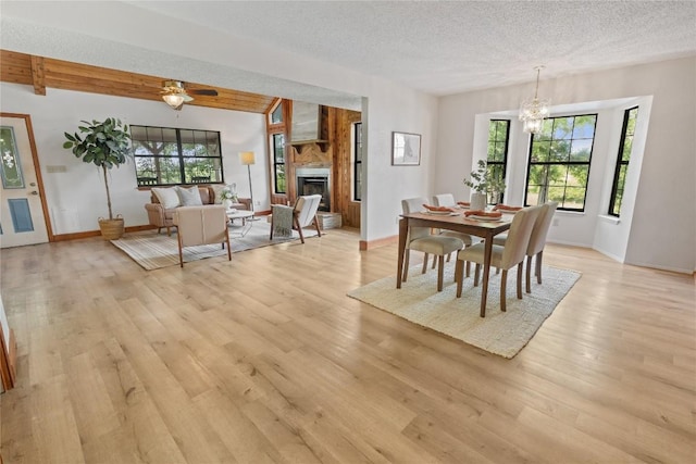 dining room featuring light wood finished floors, an inviting chandelier, a textured ceiling, and a fireplace
